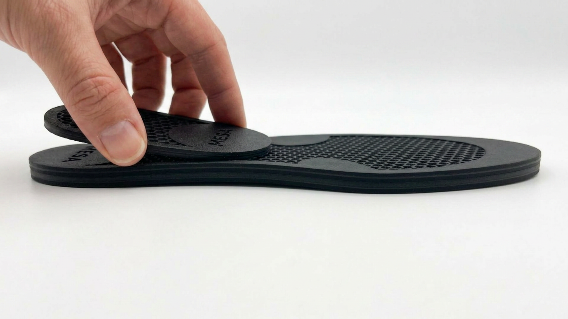 Hand removing a layer from the MESA HexLift adjustable heel lift, showing its modular interlocking design for leg length discrepancy correction